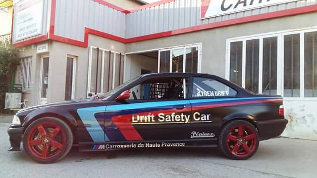 BMW noire « Drift Safety Car » aux couleurs de la Carrosserie de Haute Provence, devant l’atelier