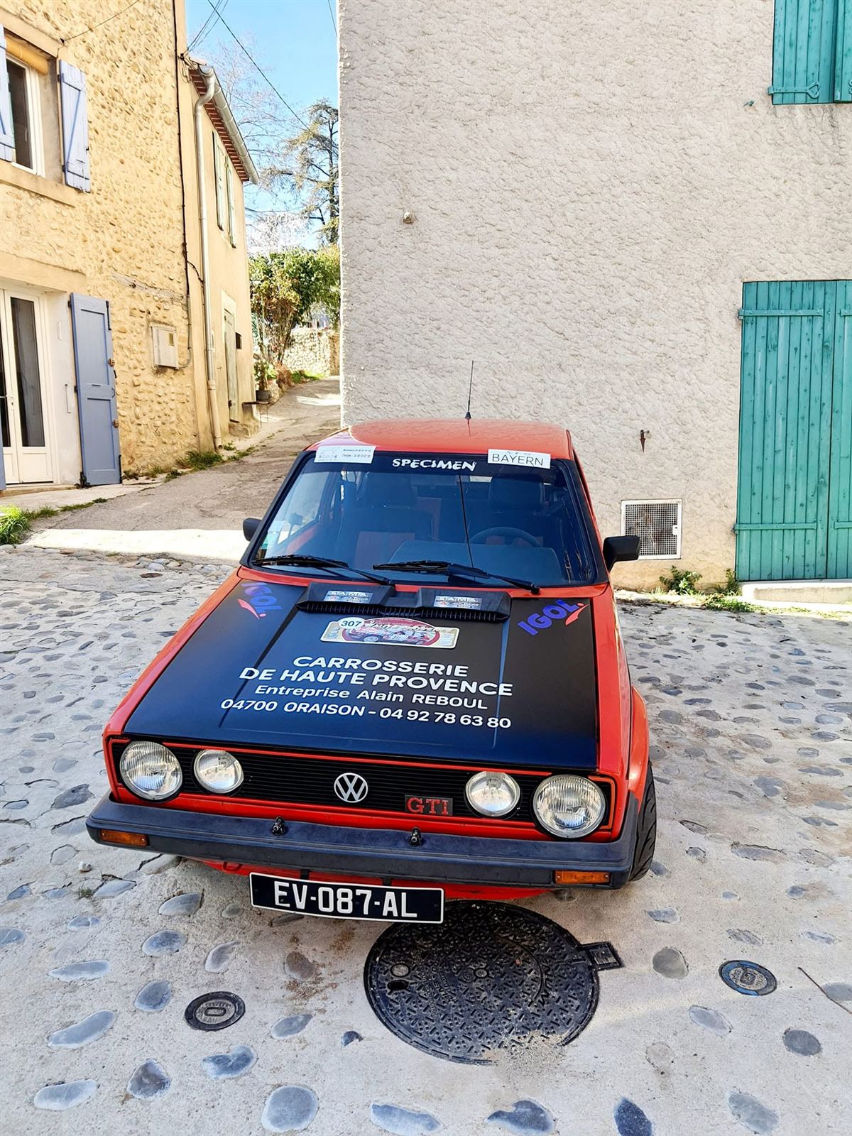 Voiture de rallye rouge et noire, numéro 307, garée devant un mur de pierre